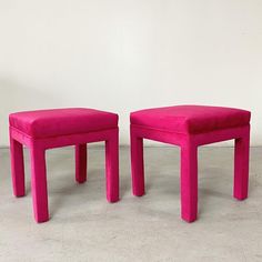 two pink stools sitting next to each other on a cement floor in front of a white wall