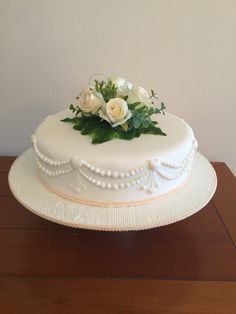 a white cake with flowers on top sitting on a wooden table next to a wall