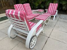 pink and white striped lawn chairs sitting next to each other on a patio with palm trees in the background