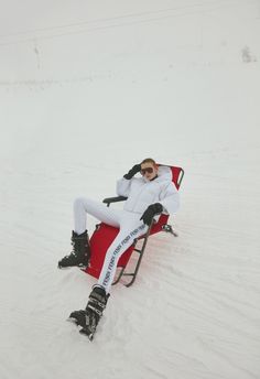 a woman sitting on top of a red chair in the snow wearing skis and goggles