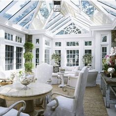 a living room filled with lots of white furniture next to tall windows and potted plants