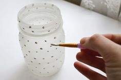 a person is holding a paintbrush in front of a glass jar with holes on it