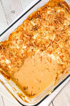 a casserole dish with cheese and other toppings in it on a white wooden table