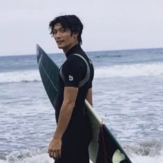 a young man holding a surfboard on top of a beach next to the ocean