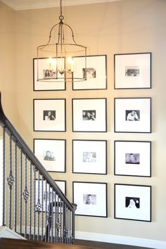 a staircase with pictures on the wall and framed photographs above it, along with a chandelier