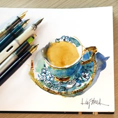 a drawing of a coffee cup and saucer with some pens on the table next to it