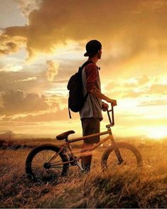 a person with a backpack standing next to a bike in a field at sunset or sunrise