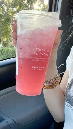 a woman is holding up a pink drink in her car