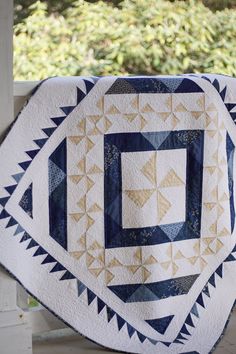 a blue and white quilt on top of a wooden fence with trees in the background