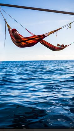 two people laying in a hammock over the ocean