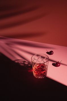 a glass filled with liquid sitting on top of a table next to two cherries