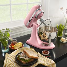 a pink mixer sitting on top of a kitchen counter next to a plate with food