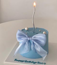 a blue birthday cake with a white bow on it and a candle in the middle