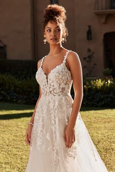 a woman in a white wedding dress standing on the grass with her hand on her hip