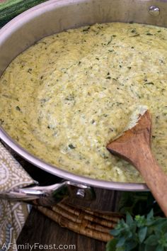 a wooden spoon in a pot filled with broccoli and cheese sauce on a table