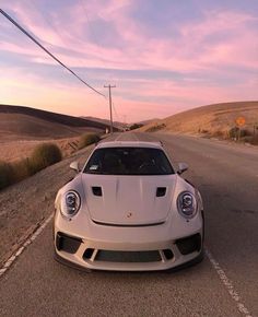 a white sports car is parked on the side of the road in front of some hills