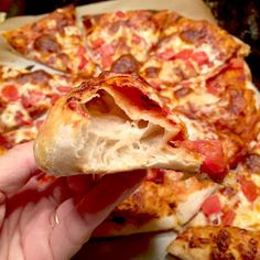 a hand holding up a slice of pizza with pepperoni and cheese toppings on it