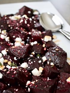 a white plate topped with cooked beets and feta cheese next to a spoon