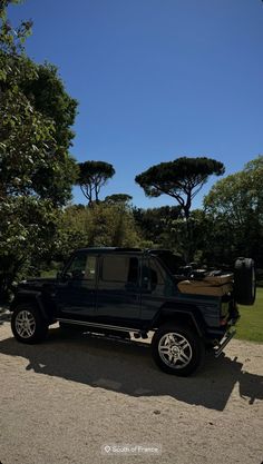 a black jeep parked on the side of a road next to trees and bushes in front of a blue sky