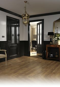 an empty room with wooden floors and black doors, chandelier hanging from the ceiling