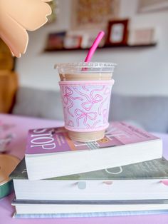 a stack of books and a cup with a pink straw on it sitting on top of each other