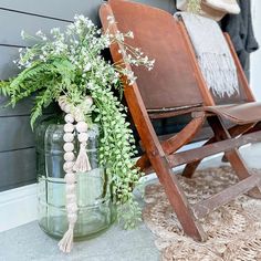 a wooden chair sitting next to a vase filled with flowers and greenery on the floor