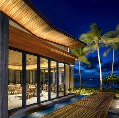 a house that is next to the ocean with palm trees in front of it at night