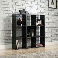 a black bookcase sitting on top of a wooden floor next to a brick wall