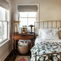 a bed sitting next to a window with a basket on top of it near a table