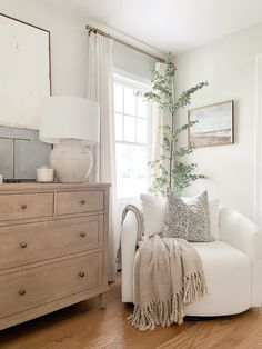 a living room filled with furniture and a white couch next to a tall plant on top of a wooden dresser