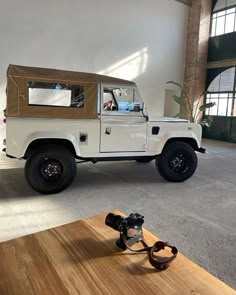 a white land rover vehicle parked in a large room with wood flooring and windows