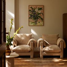 two couches in a living room with flowers on the table and paintings above them