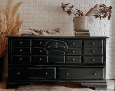 a black dresser sitting in front of a brick wall next to a potted plant