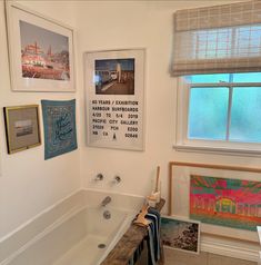 a bath tub sitting next to a window covered in pictures and framed art on the wall