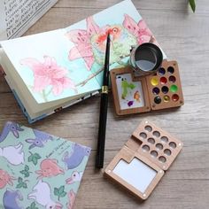 an open book with watercolors and paint on it next to other art supplies