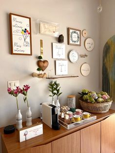 a wooden cabinet topped with lots of vases filled with flowers next to pictures on the wall