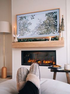 someone's feet resting on the bed in front of a fireplace with lit candles