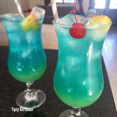 two glasses filled with blue liquid and topped with a pineapple garnish, sitting on a counter