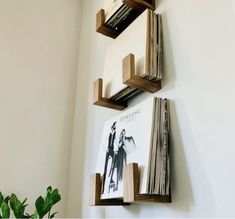 two wooden shelves holding books and magazines on the wall next to a potted plant