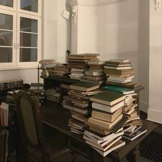 a large stack of books sitting on top of a wooden table next to a window