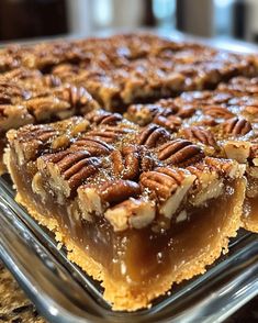 a pie with pecans on top sitting on a table next to a glass pan