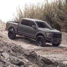 a gray truck driving down a dirt road next to some rocks and trees in the background