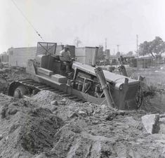 an old black and white photo of a man standing next to a bulldozer