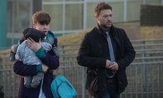 a man holding a small child in his arms while walking down the street with other people behind him