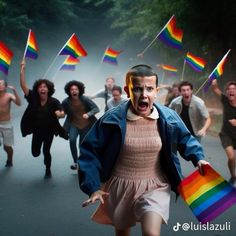 a group of people running down a road with rainbow flags in the air and one person holding a bag