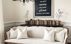 a white couch sitting under a chandelier next to a table with books on it