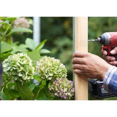 a man is using a drill to trim a wooden post with flowers in the background