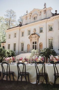 an outdoor table set up for a formal dinner in front of a large white house