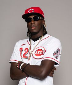 a man in a baseball uniform with his arms crossed, wearing sunglasses and a red hat