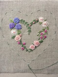 a heart made out of flowers on a piece of linen with stitching in the middle